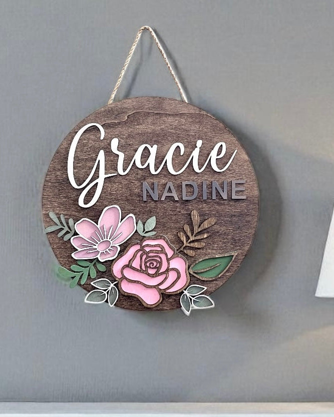 Round wooden hanging sign with floral design and custom text on a gray wall.
