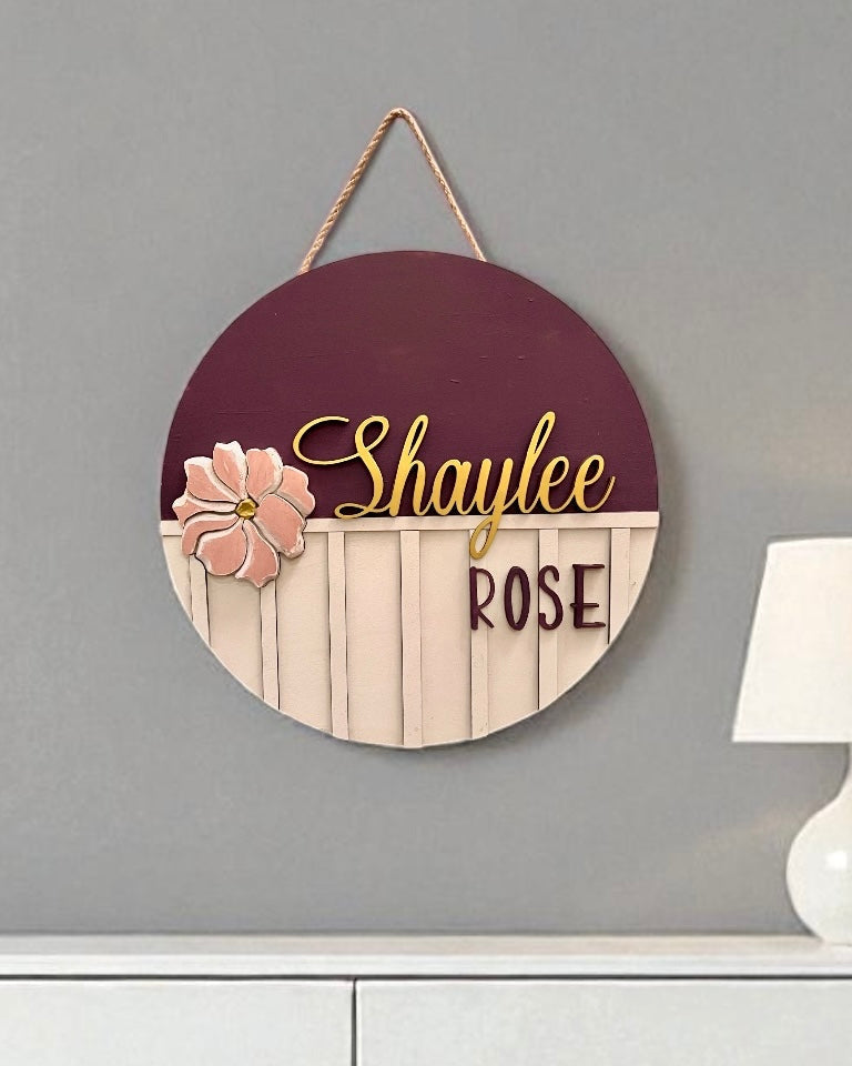 Decorative wall hanging with 'Shaylee Rose' text on a gray wall with a lamp in the background.
