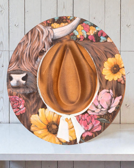 Wide brim hat with a highland cow, and floral design on a wooden background