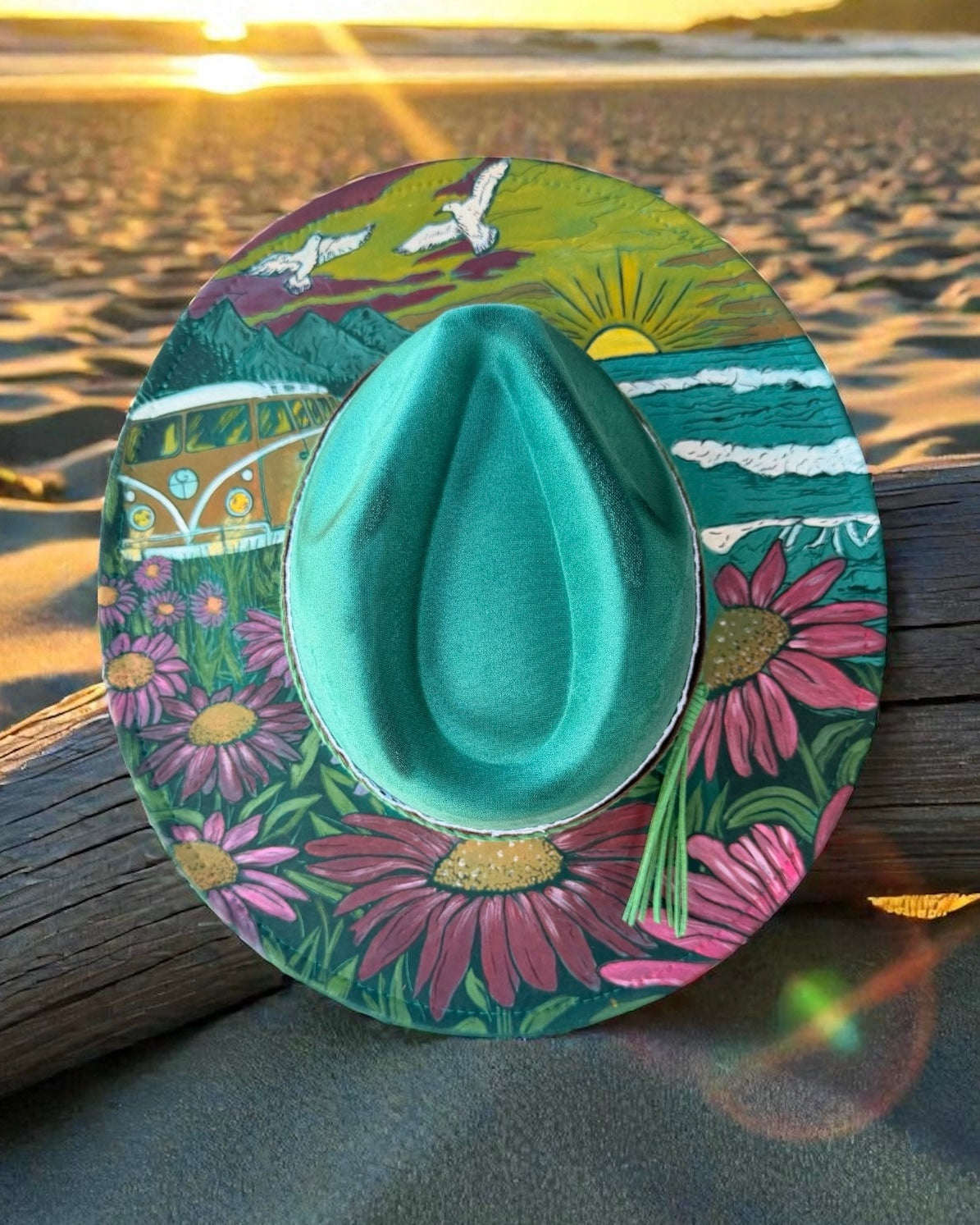 Teal cowboy hat with a colorful circular design on a beach at sunset