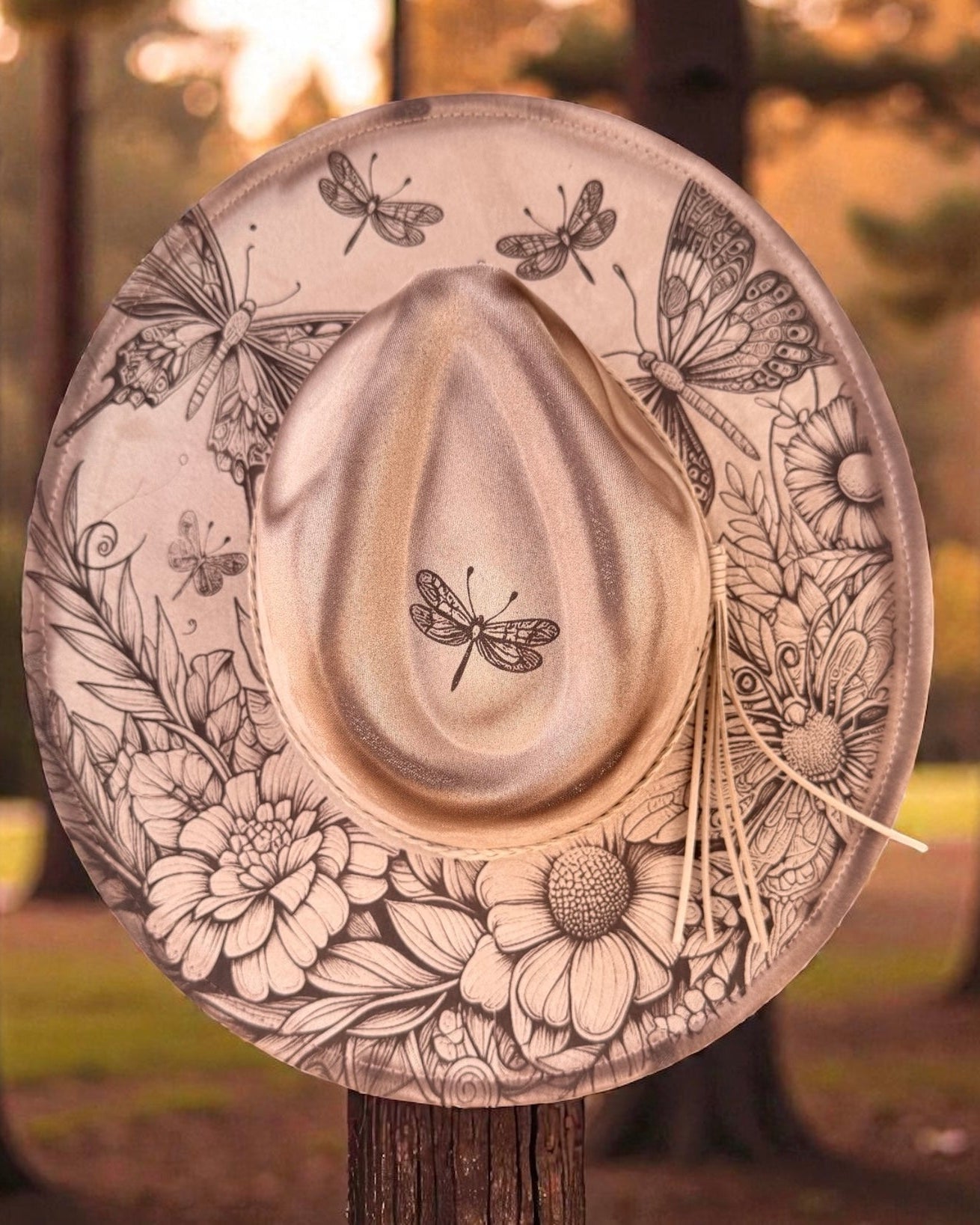 Decorative hat with butterfly and floral patterns on a wooden stand against a natural background.