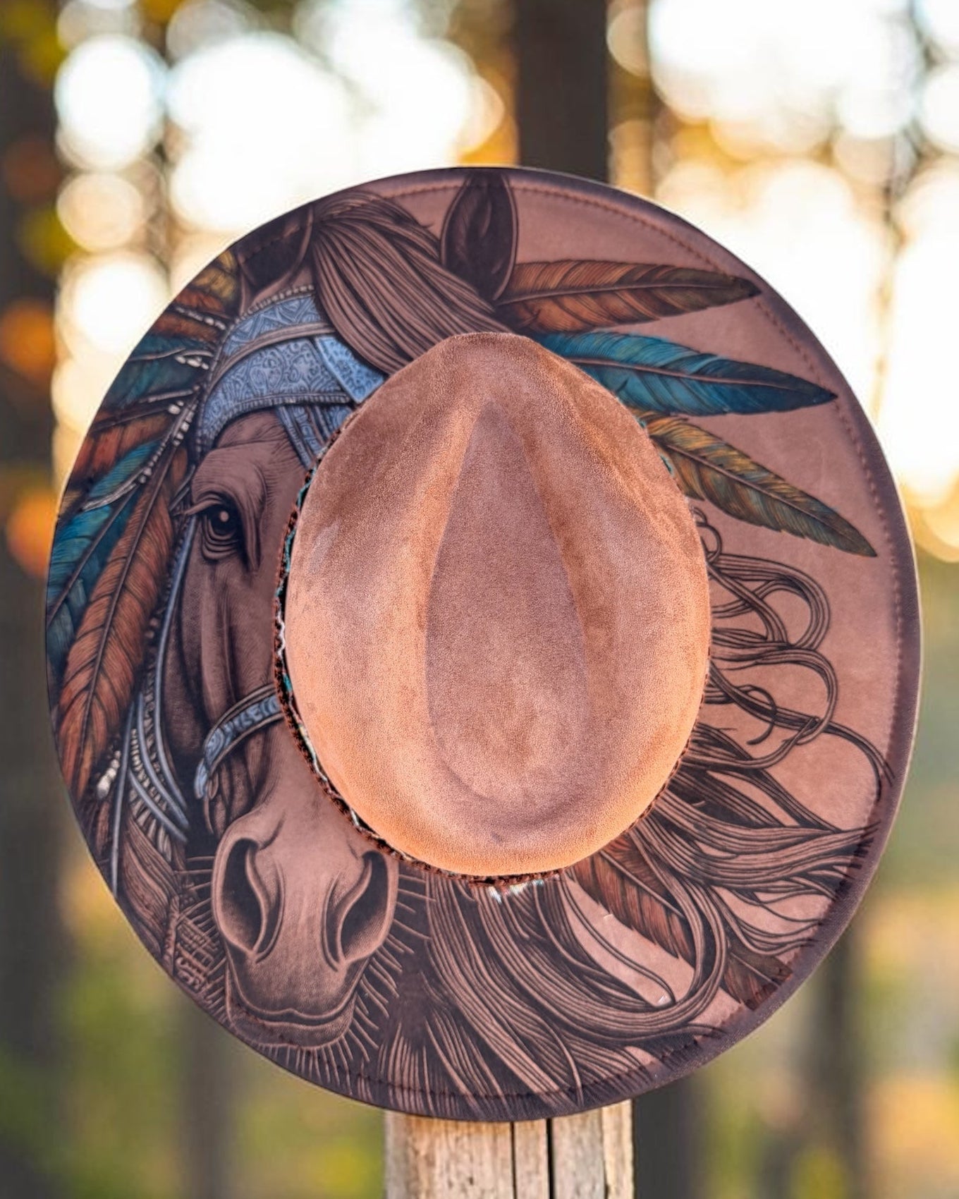 Brown cowboy hat with artistic horse design on a wooden post against a forest background