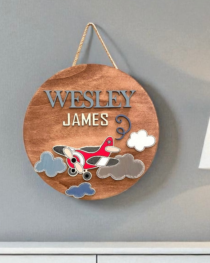 Wooden plaque with airplane design and engraved names on a gray wall.